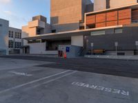 an empty parking space with large gray buildings in the background and white writing on it