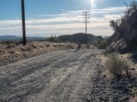 a road with dirt and gravel on it that leads into the distance with an electric pole in the foreground