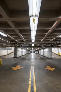 a empty parking garage with two arrow signs, and one lane sign, between the two spaces is empty,