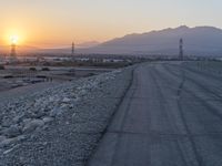 a road with gravel and power poles near some mountains at sunset over the desert area