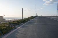 an empty road near a beach and waves as well as cars on the sand and houses on the beach