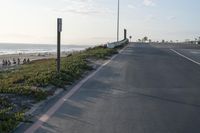 an empty road near a beach and waves as well as cars on the sand and houses on the beach