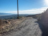 a dirt road with power lines over the valley in the background on a bright day