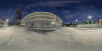 the empty skate park with concrete ramps is lit up at night time and a sky view