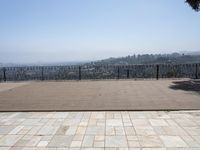 a bench overlooking a mountain city below a fence and railings as well as the ocean