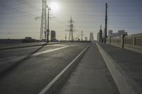 an empty highway with power lines leading to city buildings in the back ground and road tracks