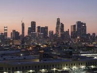 a big city skyline that is lit up at dusk in the background and pink sky