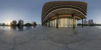 a fish eye lens panoramic view of the curved building at sunset with city in background