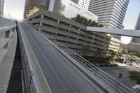 two vehicles drive down a city road next to tall buildings and a parking garage overpass