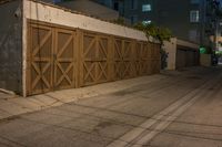 a wooden garage door sitting in front of a building at night with lights on the ground