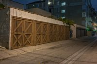 a wooden garage door sitting in front of a building at night with lights on the ground