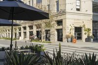 several tables with umbrellas outside an empty store front on a city street with cactus