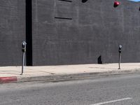 two parking meters in front of a large grey wall with several red light at the top of them