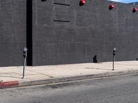 two parking meters in front of a large grey wall with several red light at the top of them