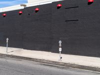 two parking meters in front of a large grey wall with several red light at the top of them