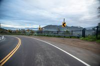 a highway has two yellow traffic signs at the end of the street, and a black gate on the other side