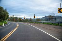 a highway has two yellow traffic signs at the end of the street, and a black gate on the other side