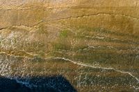 an aerial shot of a person riding a surfboard on the ocean shore line along with a beach in the background