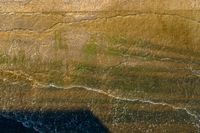 an aerial shot of a person riding a surfboard on the ocean shore line along with a beach in the background