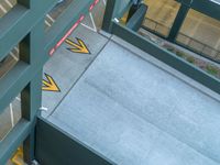 two yellow arrows pointing in opposite directions on a ramp, next to an alley way