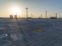 an empty parking lot during the sunset with broken yellow arrow marks on concrete and pole lights