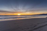 a heart shape drawn in the sand on a beach as the sun sets behind a large mountain