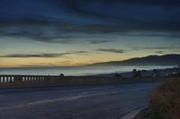 the coast with waves is at the right of this photo, a person riding his motorcycle on the street