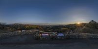 the sun is setting behind a stone wall that covers a bench on a hillside overlooking a city