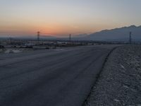 a lone motorcycle on the side of a road during sunset with mountains in the background