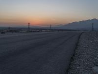 a lone motorcycle on the side of a road during sunset with mountains in the background