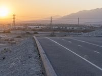 a motorcycle sits parked on a gravel path near the road with the sun setting behind it