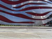 a man is riding a skateboard on the sidewalk by an artistic building that is red and white