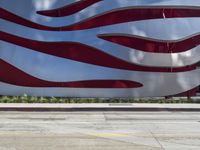 a man is riding a skateboard on the sidewalk by an artistic building that is red and white