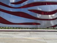 a man is riding a skateboard on the sidewalk by an artistic building that is red and white