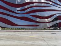 a man is riding a skateboard on the sidewalk by an artistic building that is red and white