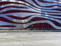 a man is riding a skateboard on the sidewalk by an artistic building that is red and white