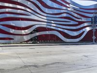 a man is riding a skateboard on the sidewalk by an artistic building that is red and white