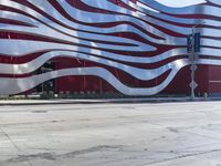 a man is riding a skateboard on the sidewalk by an artistic building that is red and white