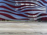 a man is riding a skateboard on the sidewalk by an artistic building that is red and white