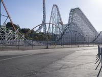 the empty amusement park with its roller coaster and ride in view, near a parking lot