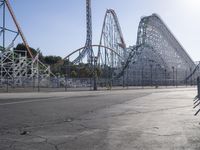 the empty amusement park with its roller coaster and ride in view, near a parking lot