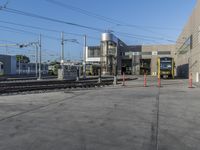 a yellow train pulling into a rail yard next to tall buildings and tracks with overhead power lines