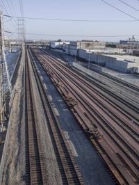 several train tracks run alongside each other next to a warehouse building and electric poles, in front of large buildings,