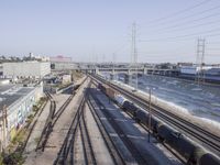 several train tracks run alongside each other next to a warehouse building and electric poles, in front of large buildings,