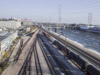 several train tracks run alongside each other next to a warehouse building and electric poles, in front of large buildings,