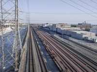 several train tracks run alongside each other next to a warehouse building and electric poles, in front of large buildings,