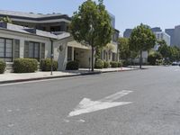 an arrow is pointing to an empty street next to buildings with green trees lining both sides