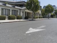 an arrow is pointing to an empty street next to buildings with green trees lining both sides