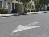 an arrow is pointing to an empty street next to buildings with green trees lining both sides