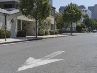 an arrow is pointing to an empty street next to buildings with green trees lining both sides